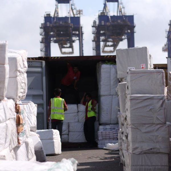 Dock workers loading cargo at Karachi Port with visible cranes and containers.