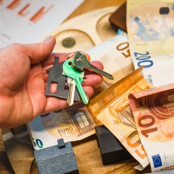A hand holding house keys over euro banknotes, symbolizing real estate and finance.